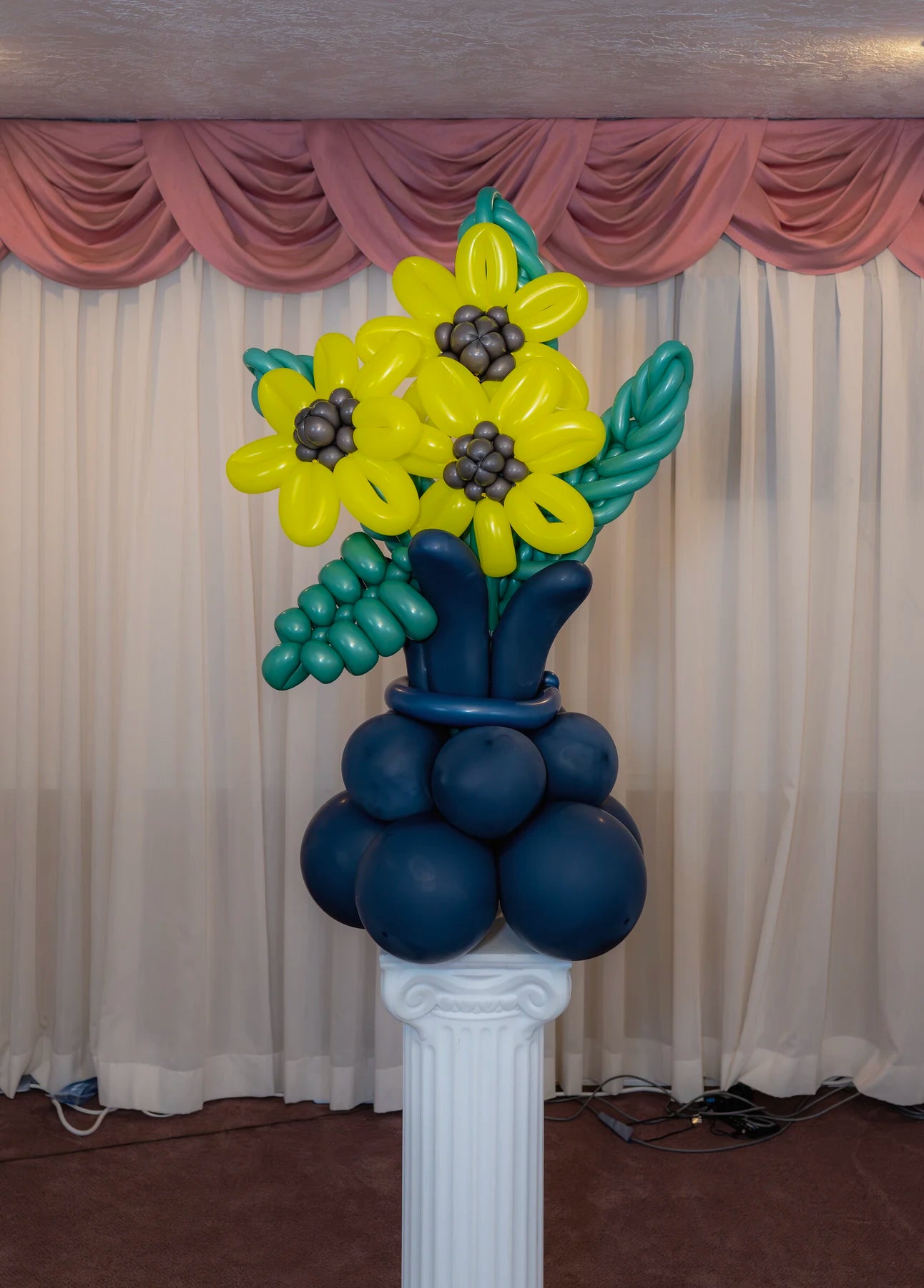 Yellow sunflower-style balloon bouquet arranged in a dark blue balloon vase.
