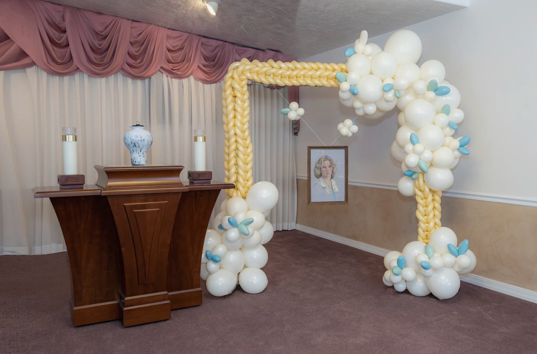 Cream and gold memorial balloon arch framing a portrait display.