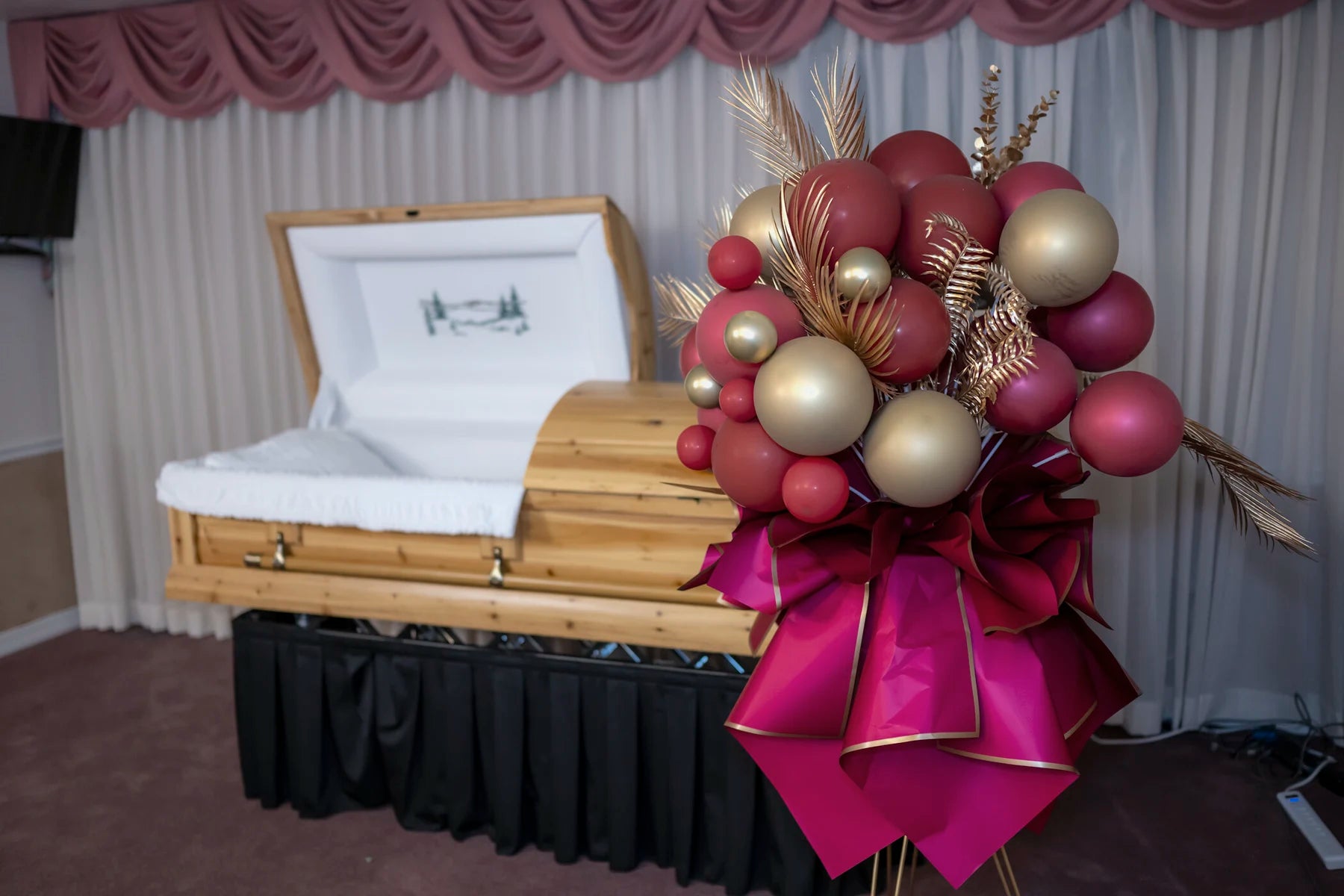 Burgundy and gold memorial standing arrangement beside a casket.