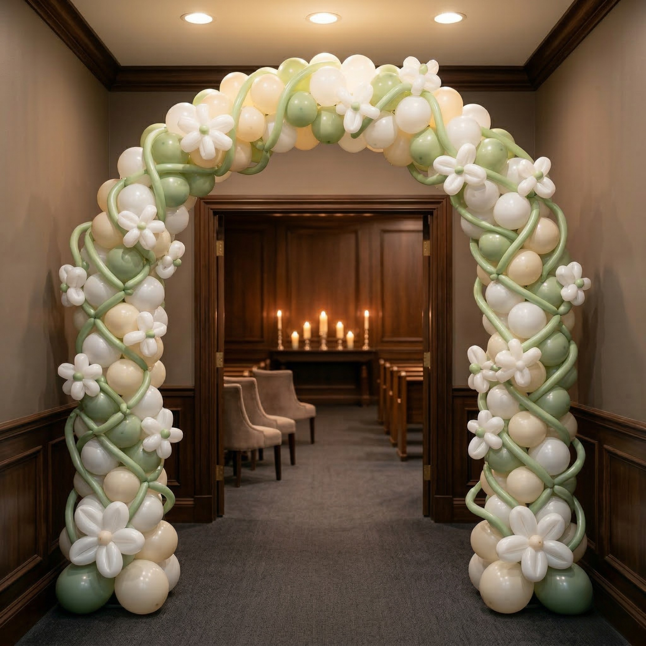 A sage green and cream doorway arch with white lattice-weave columns and white daisy flowers, framing a candlelit chapel with wooden pews through the doorway